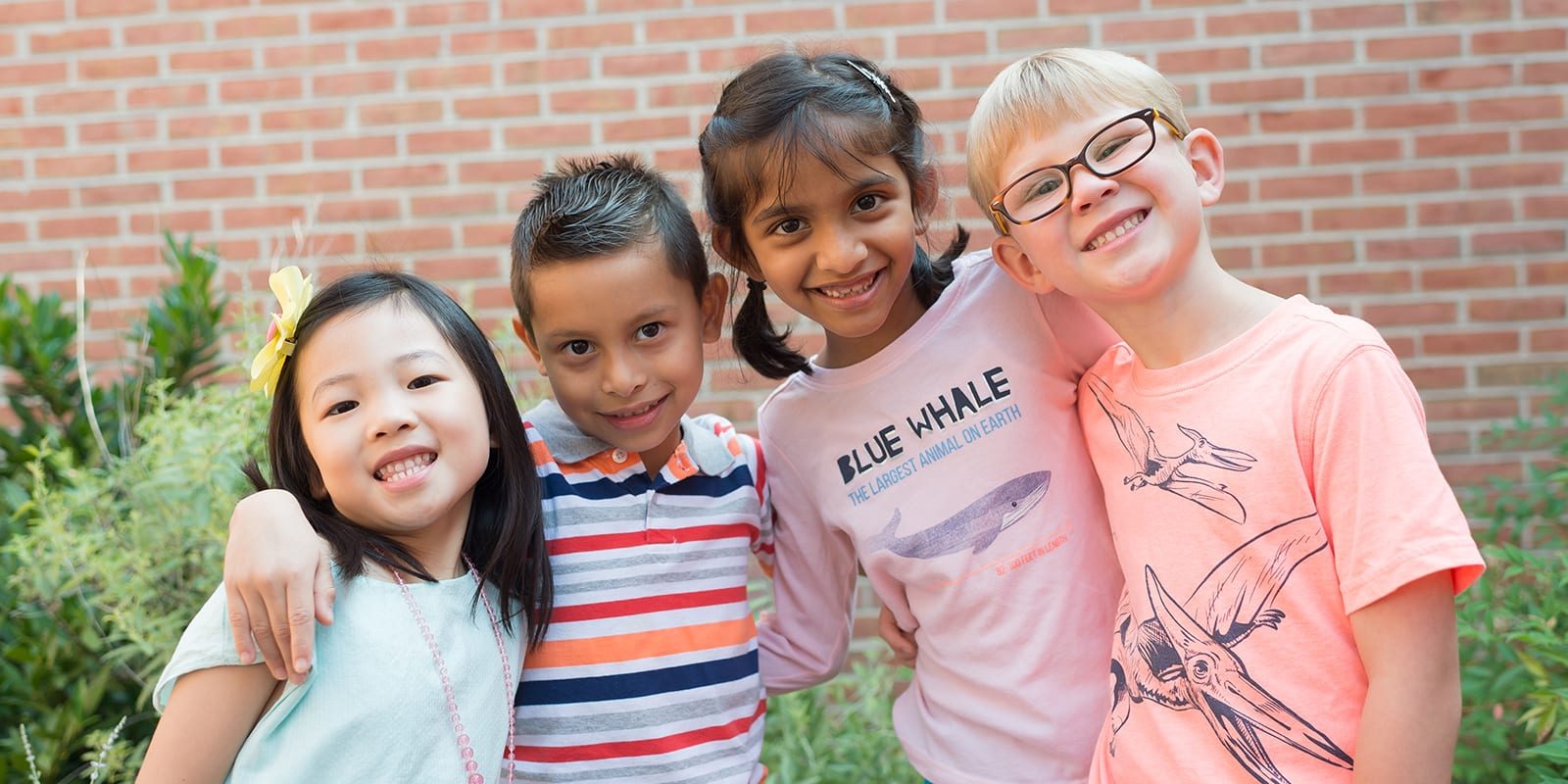 Photo of four young students smiling at the camera arm in arm